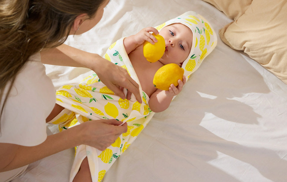 Baby wrapped in a lemon print hooded towel after bath time