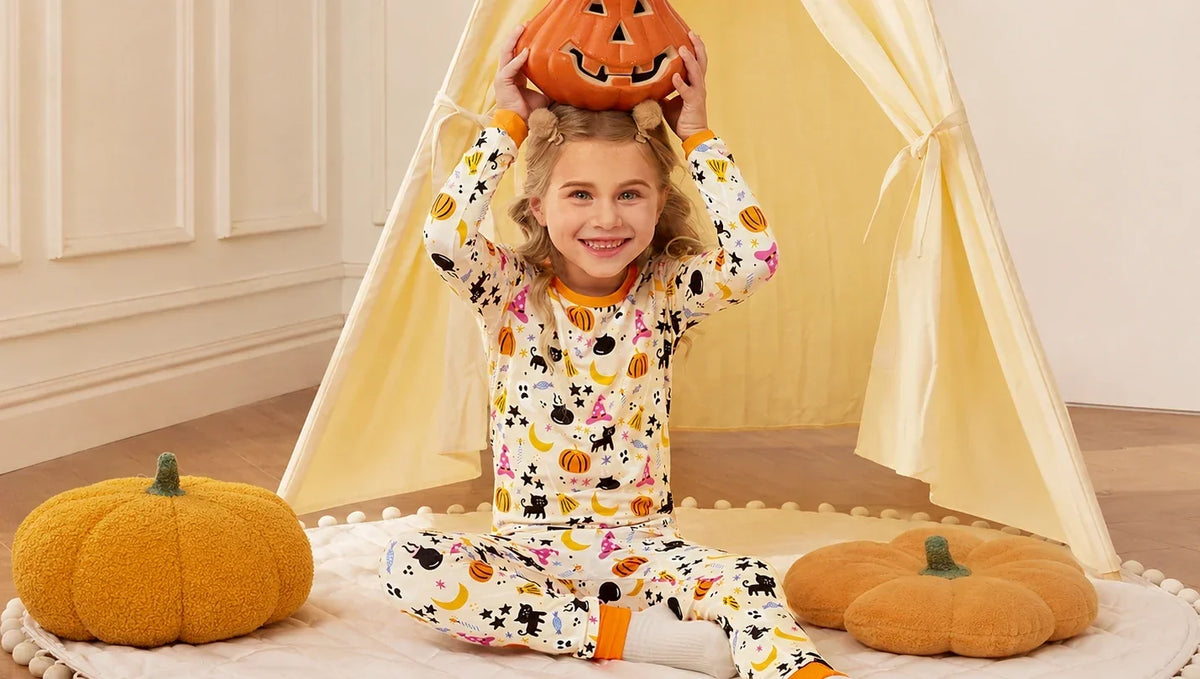 Child wearing Halloween pajamas while sitting with pumpkin decorations