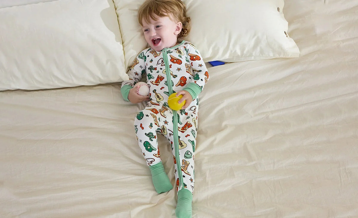 A toddler sitting awake on a bed in animal-print pajamas with mint-green cuffs