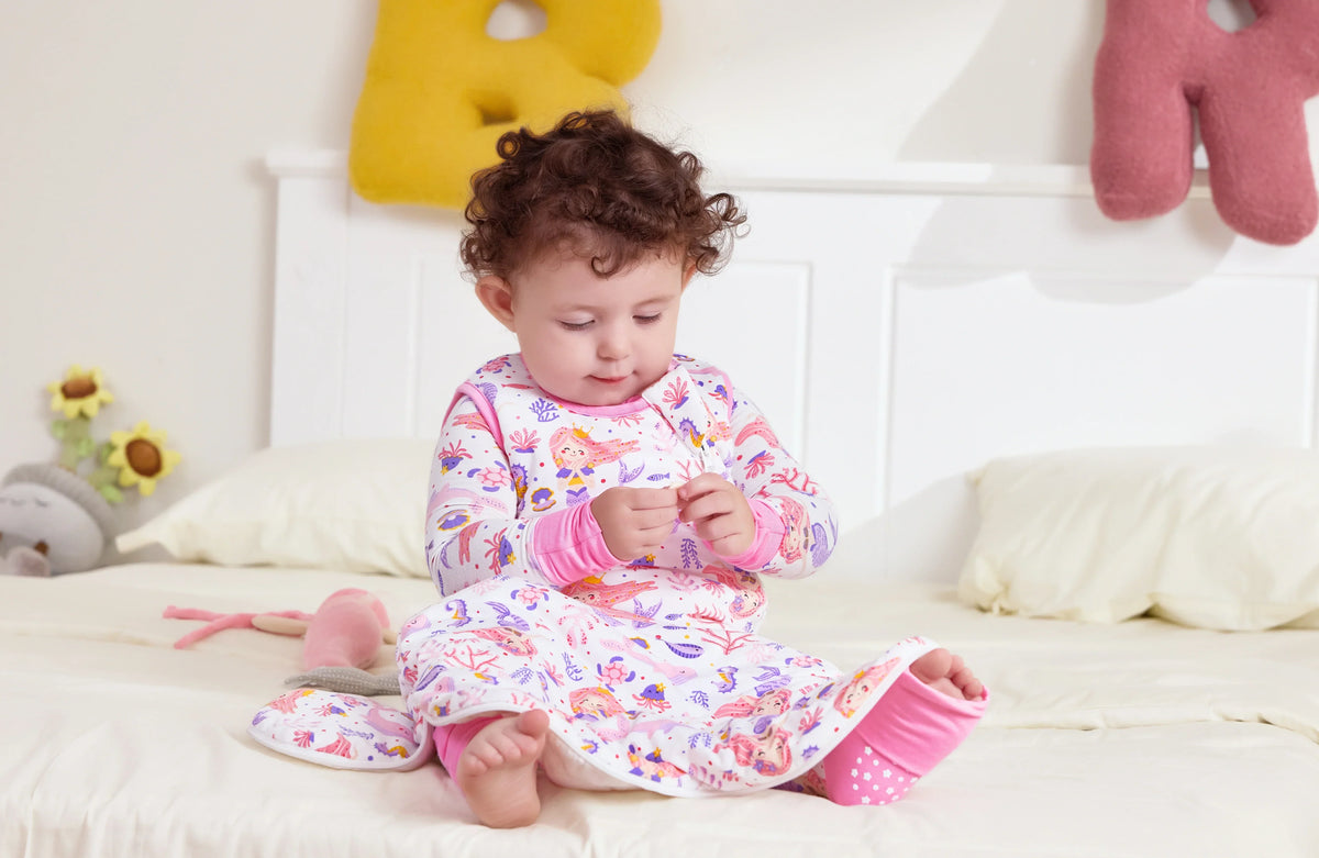 Toddler sitting on a bed in a bamboo sleep sack before bedtime