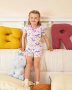 Lavender Unicorn Short Two-Piece Pajama Set - child wearing the short pajamas while seated on a bed