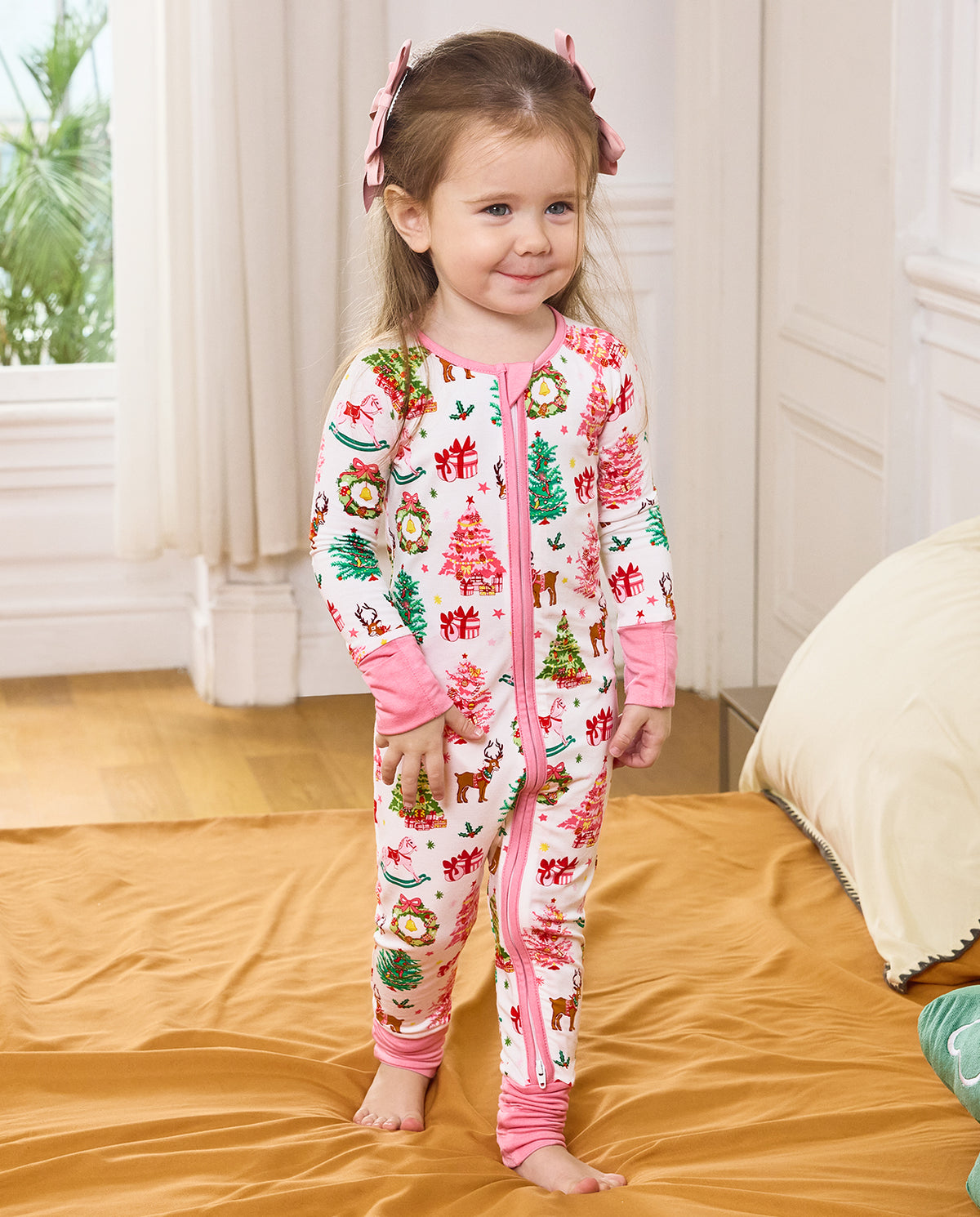 Child standing on orange bedding in the white Blush Christmas zip-up romper.