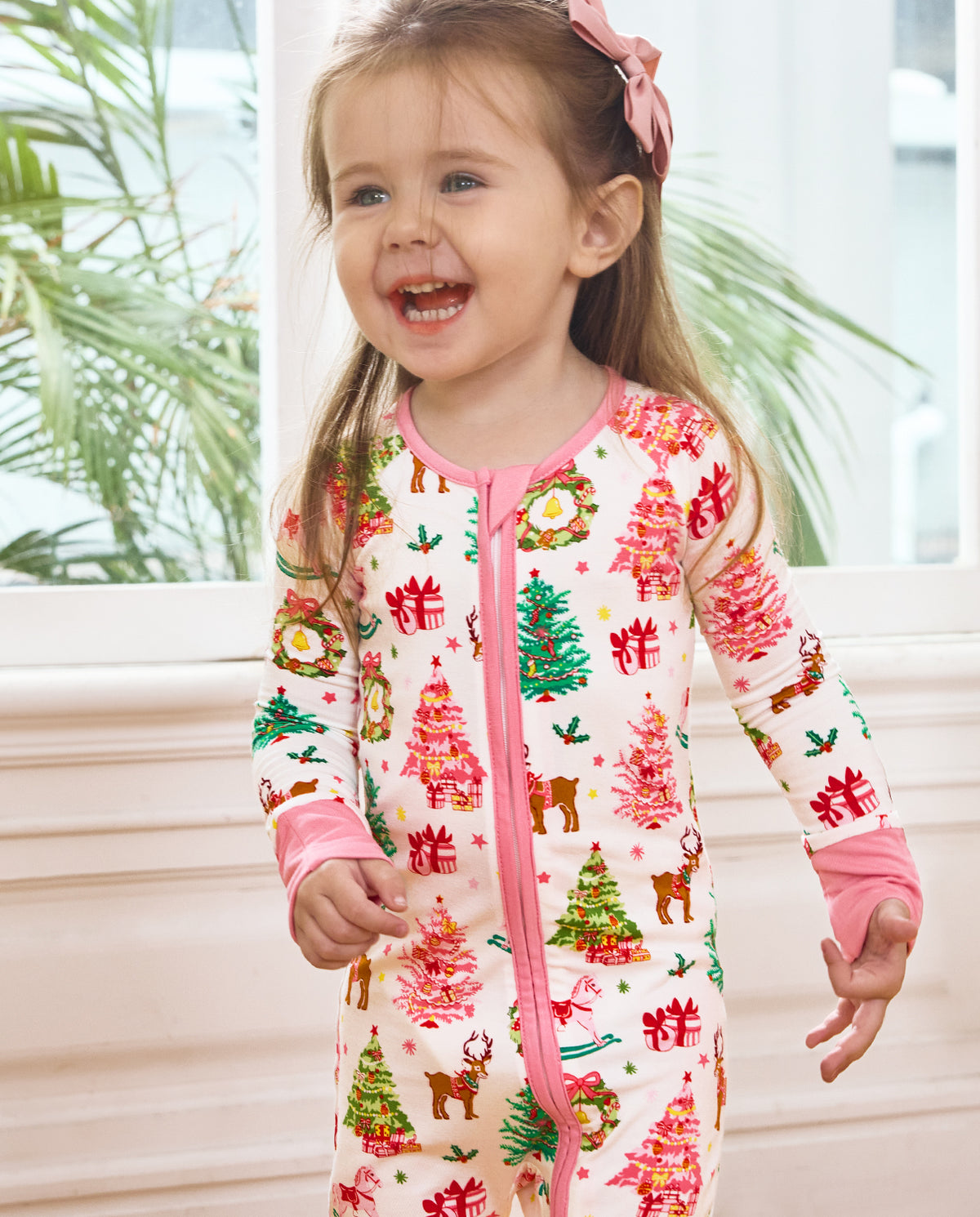 Close front view of a smiling child standing in the Blush Christmas romper.
