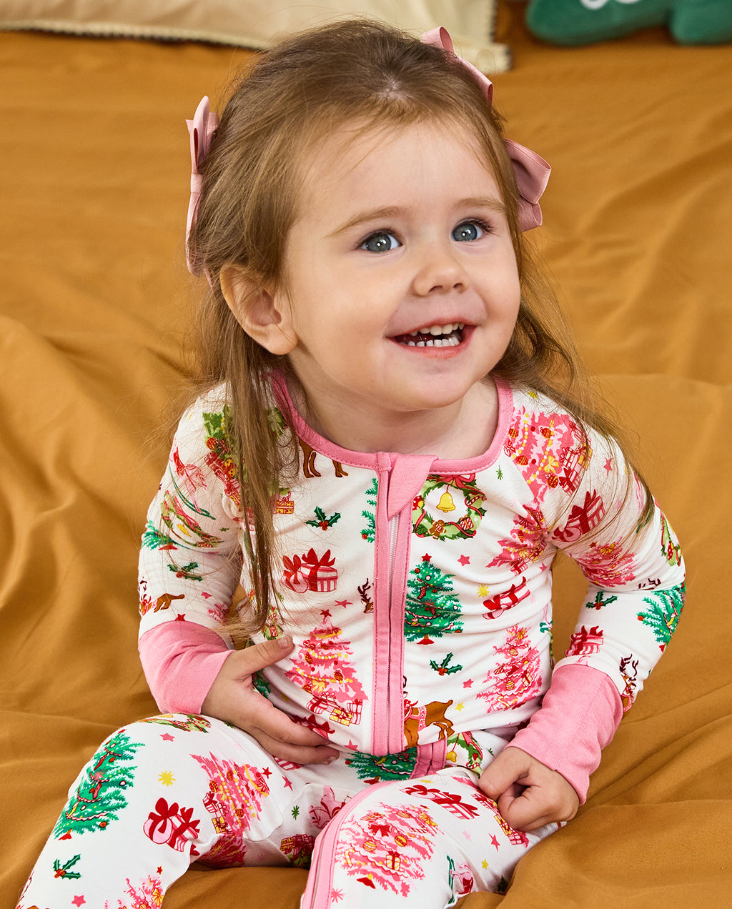 Child seated on bedding smiling in the Blush Christmas romper with pink cuffs.