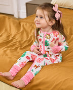 Child seated on orange bedding in the Blush Christmas romper with uncovered feet.