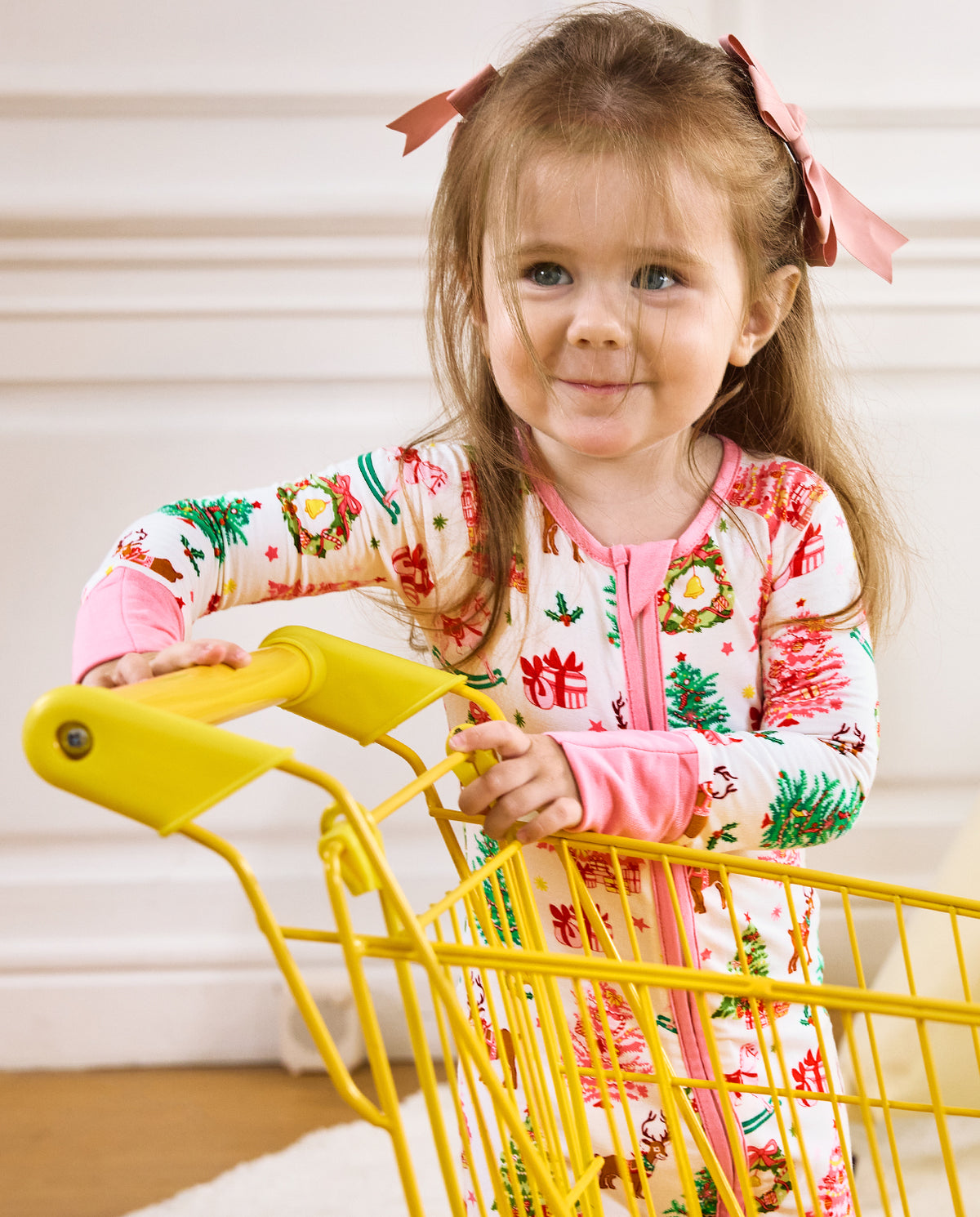 Child holding a yellow cart handle in the white Blush Christmas romper.