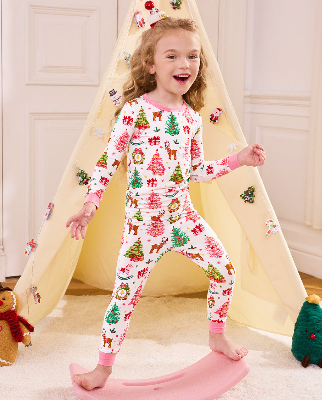 Child standing on a slide with a hand raised in Blush Christmas pajamas.