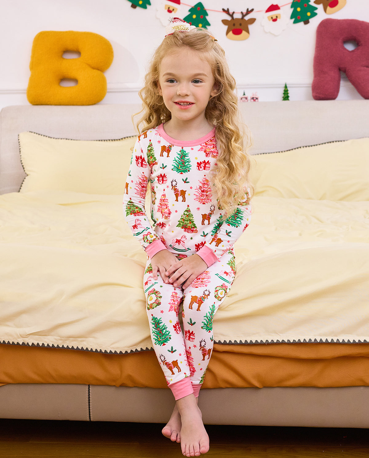 Child seated on bedding with crossed legs in Blush Christmas pajamas.