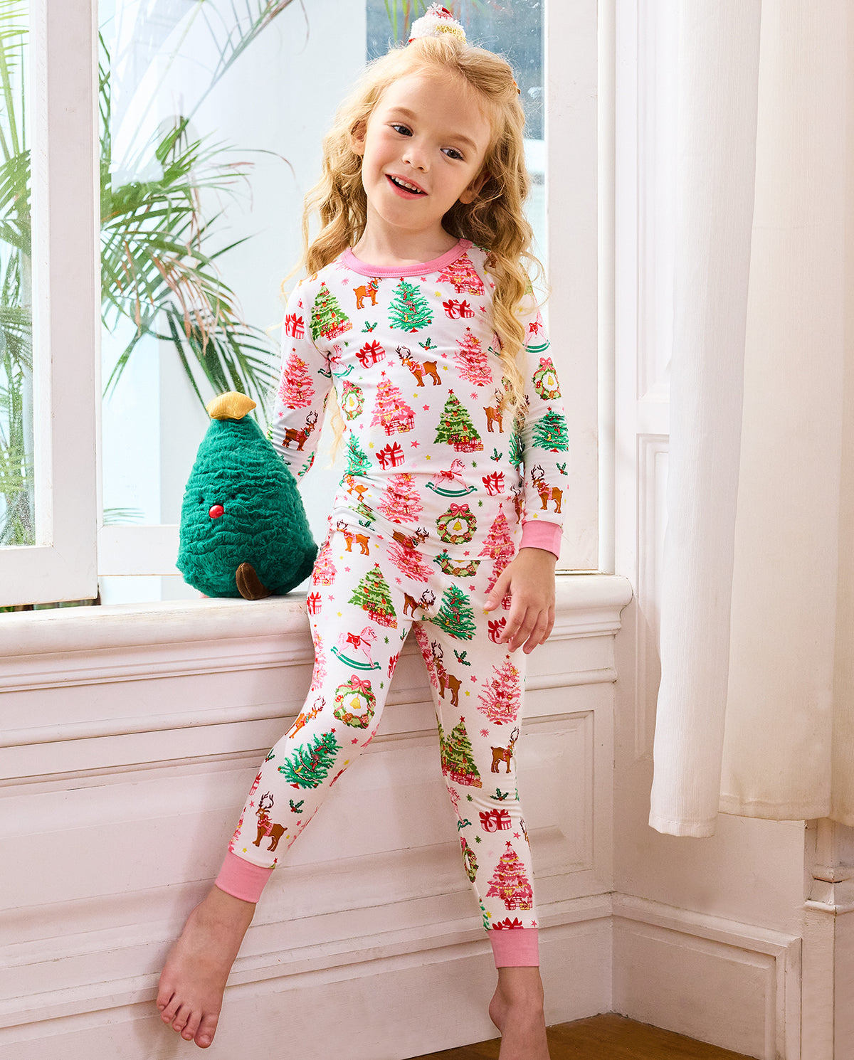 Child standing beside a window in Blush Christmas pajamas with pink cuffs.