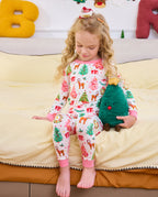 Child looking down and holding a plush tree while seated on a sofa in Blush Christmas pajamas.