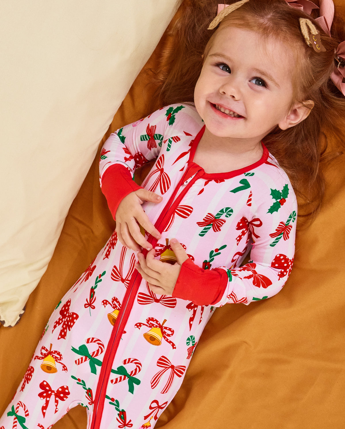 Child reclining on orange bedding in the Christmas Bow zip-up romper.