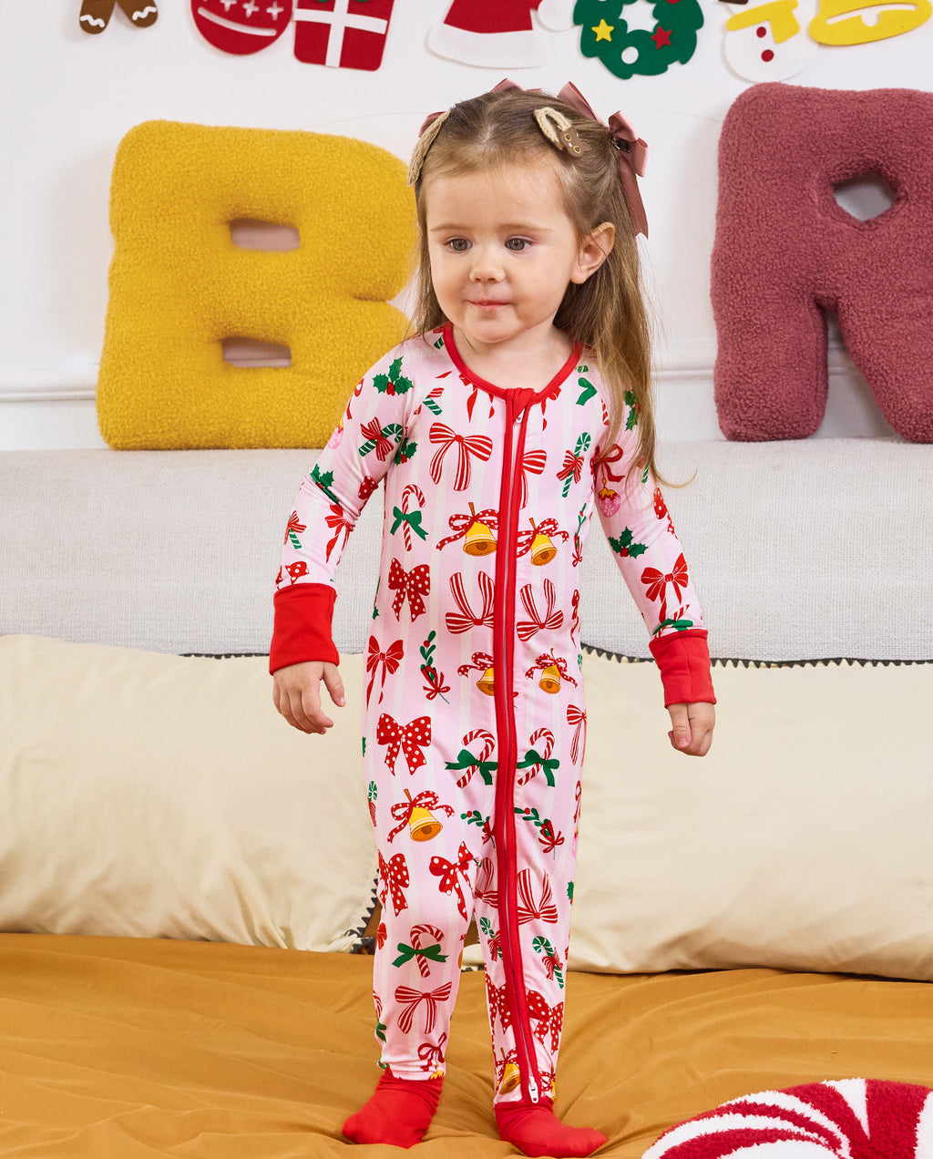 Child standing on bedding in the Christmas Bow romper with red cuffs.