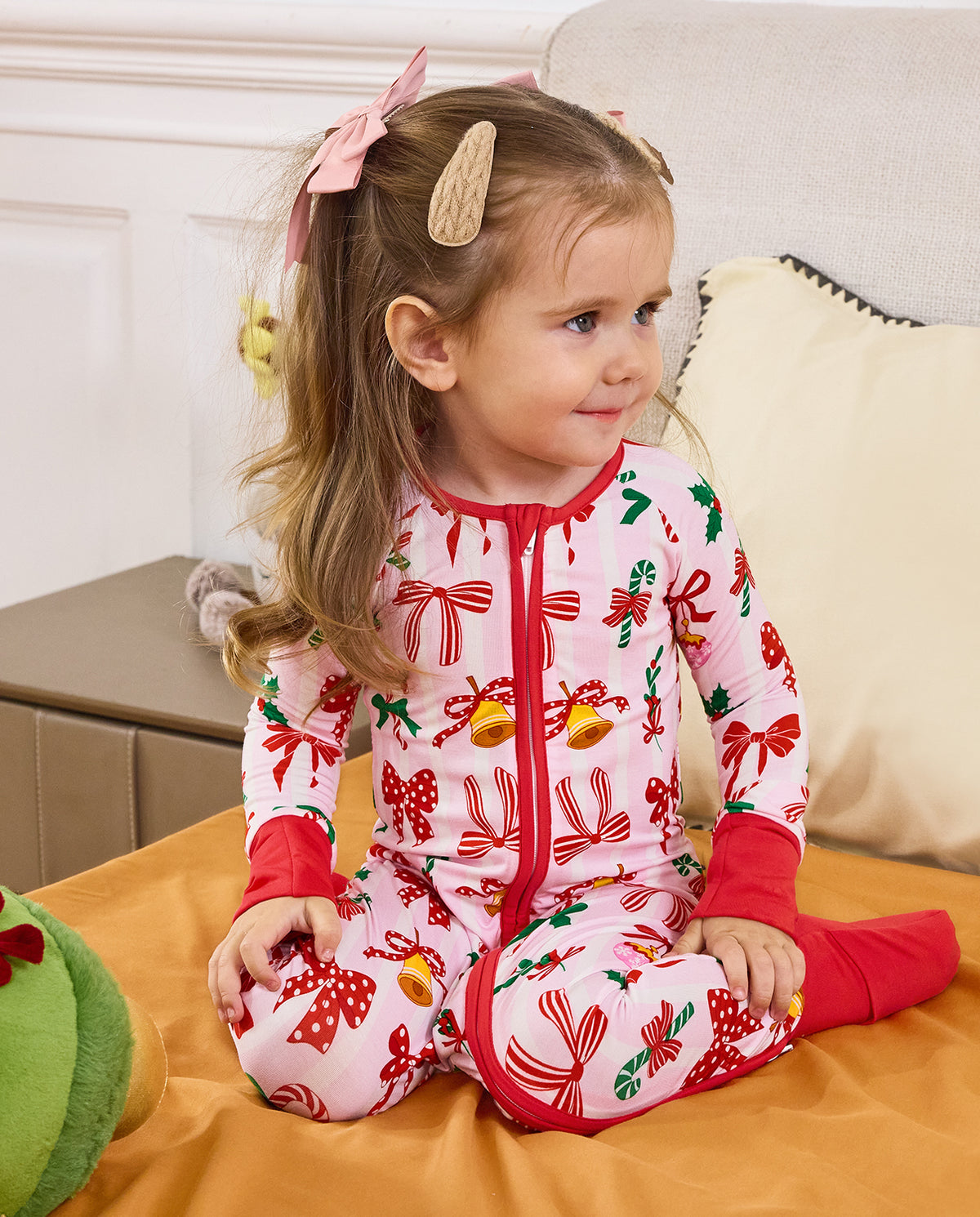 Child seated beside a sofa in the Christmas Bow zip-up romper.