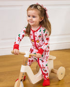 Child seated on a wooden tricycle holding the handle in the Christmas Bow romper.