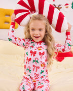 Child holding red and white plush candy canes overhead in Christmas Bow pajamas.