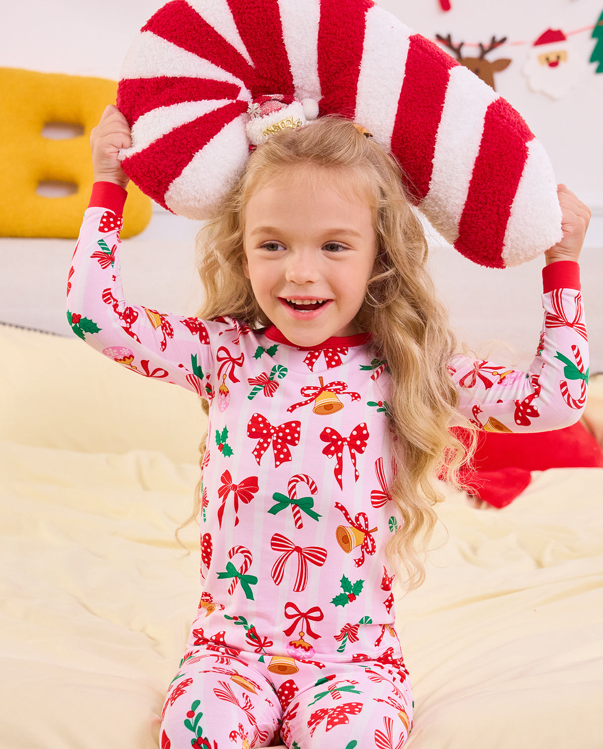 Child holding red and white plush candy canes overhead in Christmas Bow pajamas.