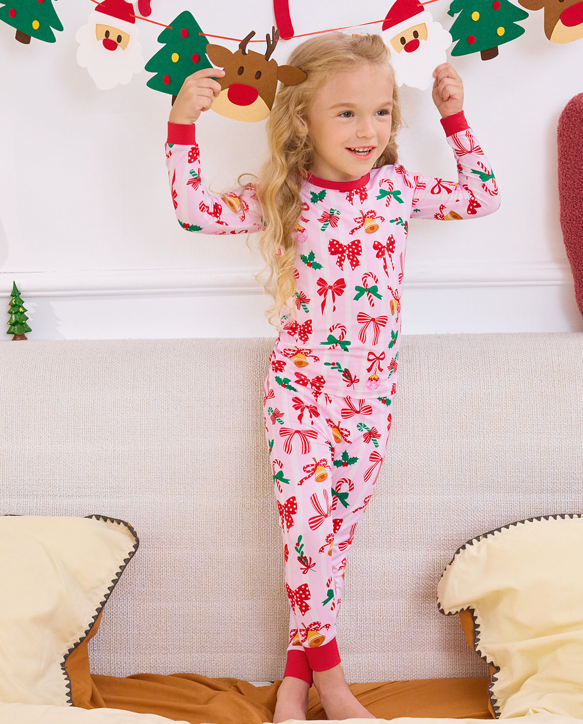 Child standing on a sofa with hands raised in Christmas Bow pajamas.