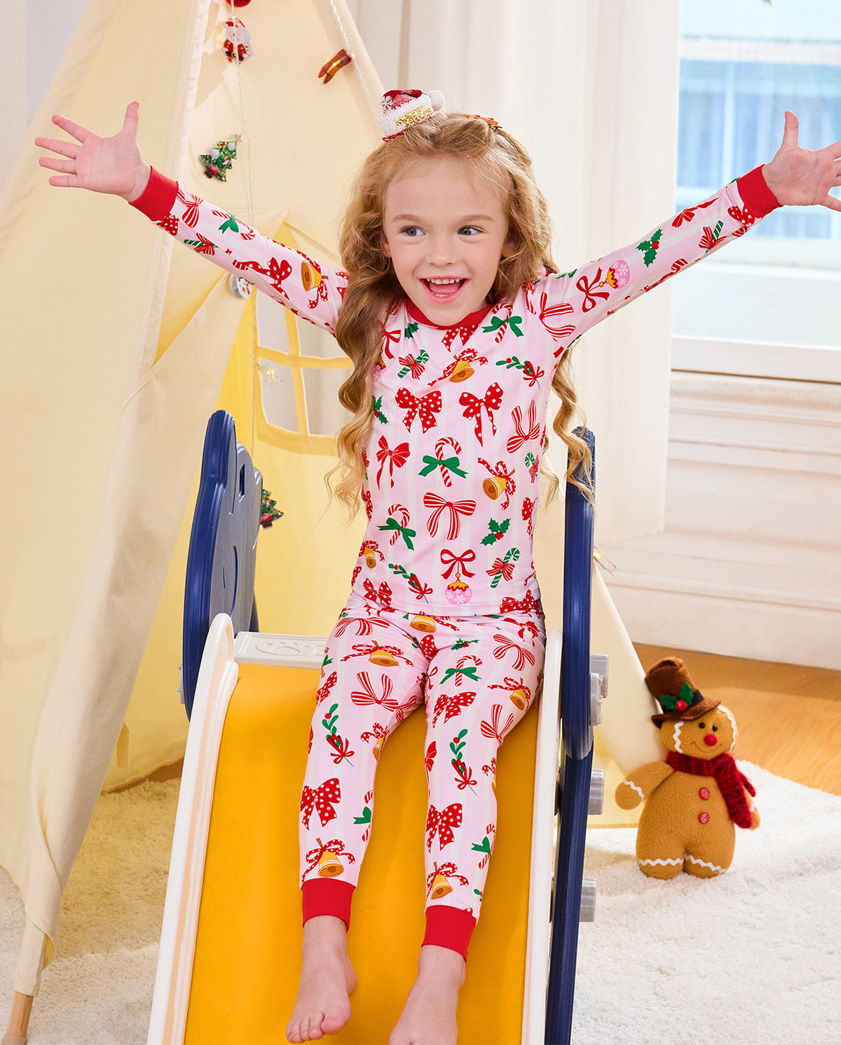 Child standing on a slide with arms out in Christmas Bow pajamas.