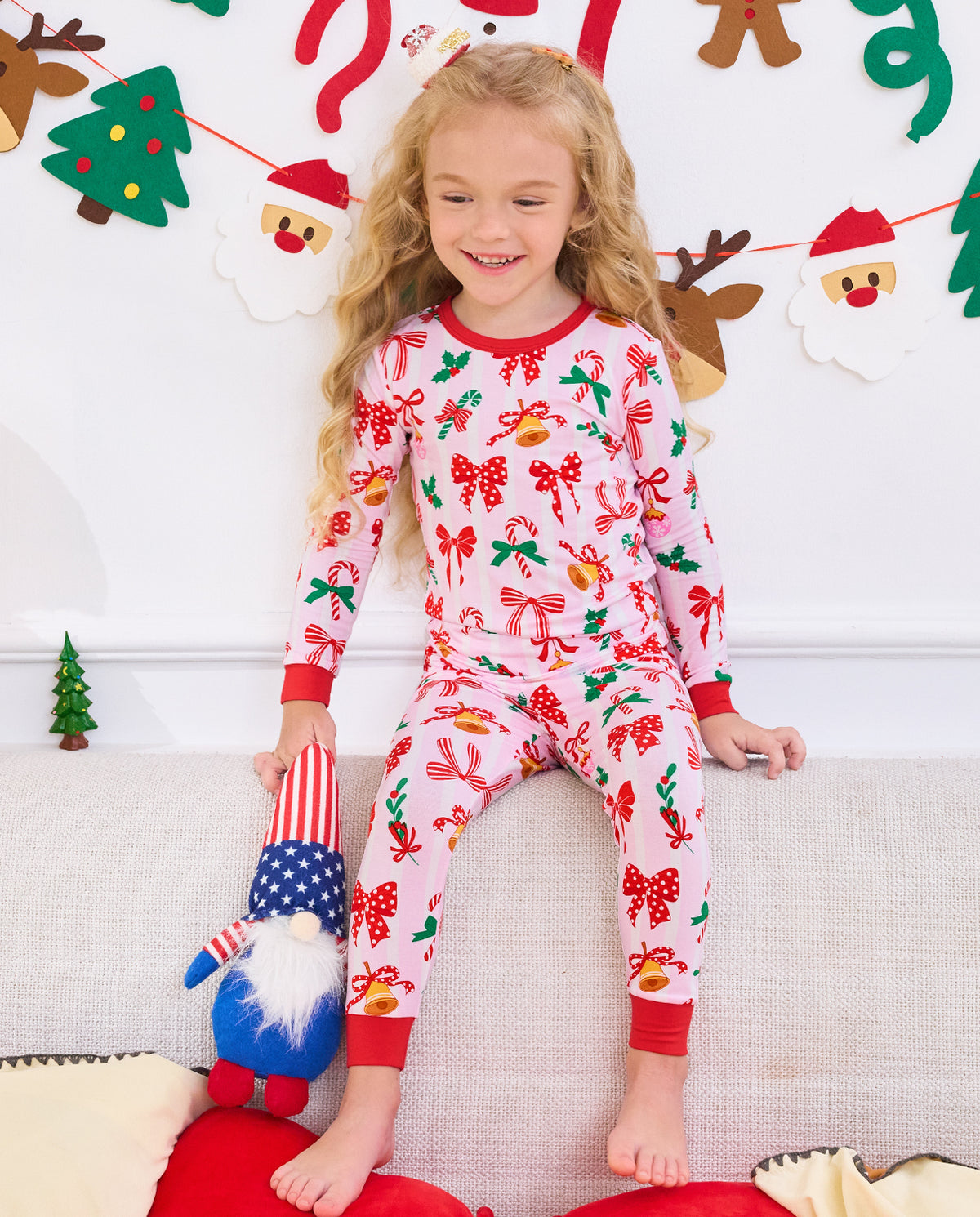Child seated on a sofa with a plush toy in Christmas Bow pajamas.