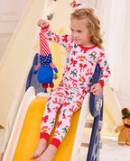 Child seated on a slide holding a plush toy in Christmas Bow pajamas.