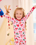Child seated with arms raised and a plush toy in Christmas Bow pajamas.
