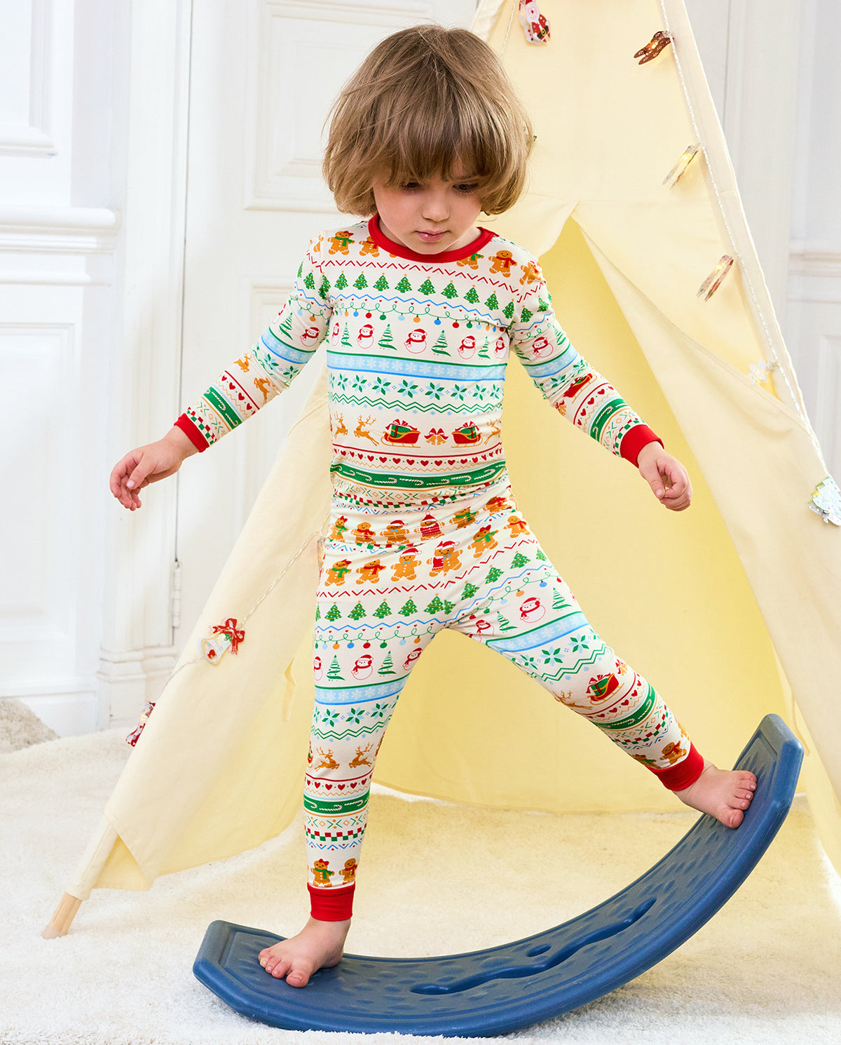 Child wearing Christmas Fair Isle pajamas while standing beside a blue rocking toy
