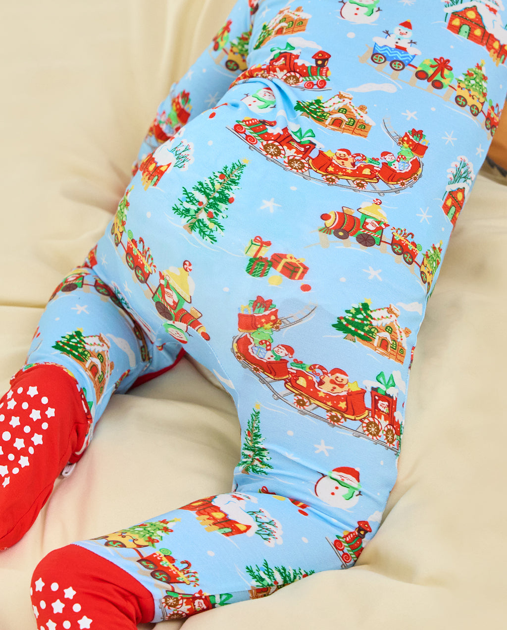 Close-up of the Christmas Trains Bamboo Zippy on a reclining child, showing Santa trains, gifts and Christmas trees above the red footies.