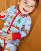 Child wearing the light blue Christmas Trains Bamboo Zippy with red zipper and cuffs, smiling in a close-up front view.