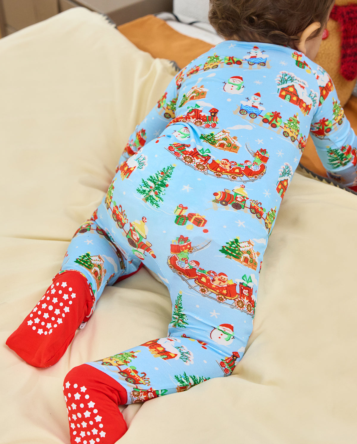 Rear view of a child reclining on a pale sofa in the Christmas Trains Bamboo Zippy, showing the light blue print and red covered feet.