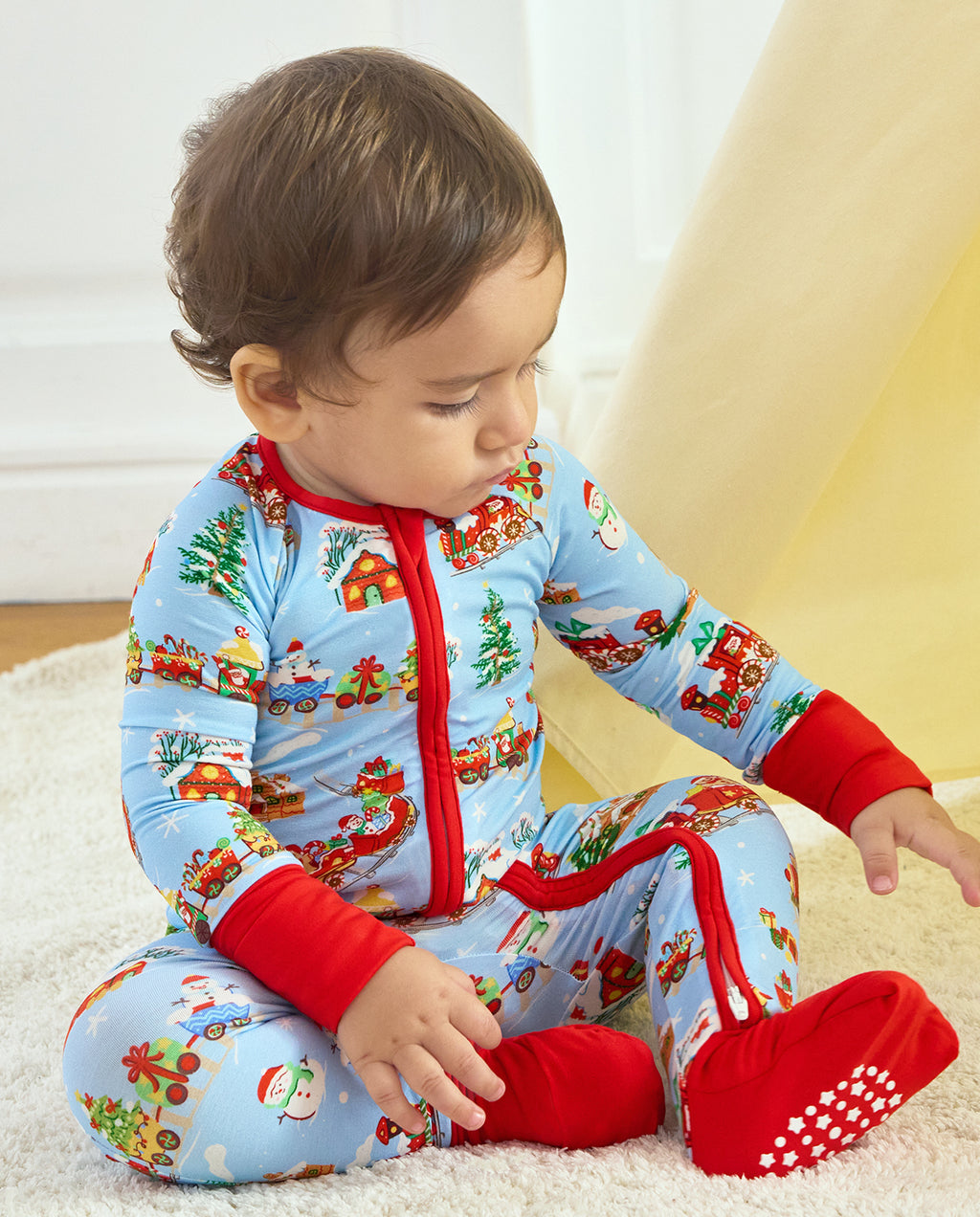 Child looking down while seated in the Christmas Trains Bamboo Zippy, showing the red zipper and covered footies.