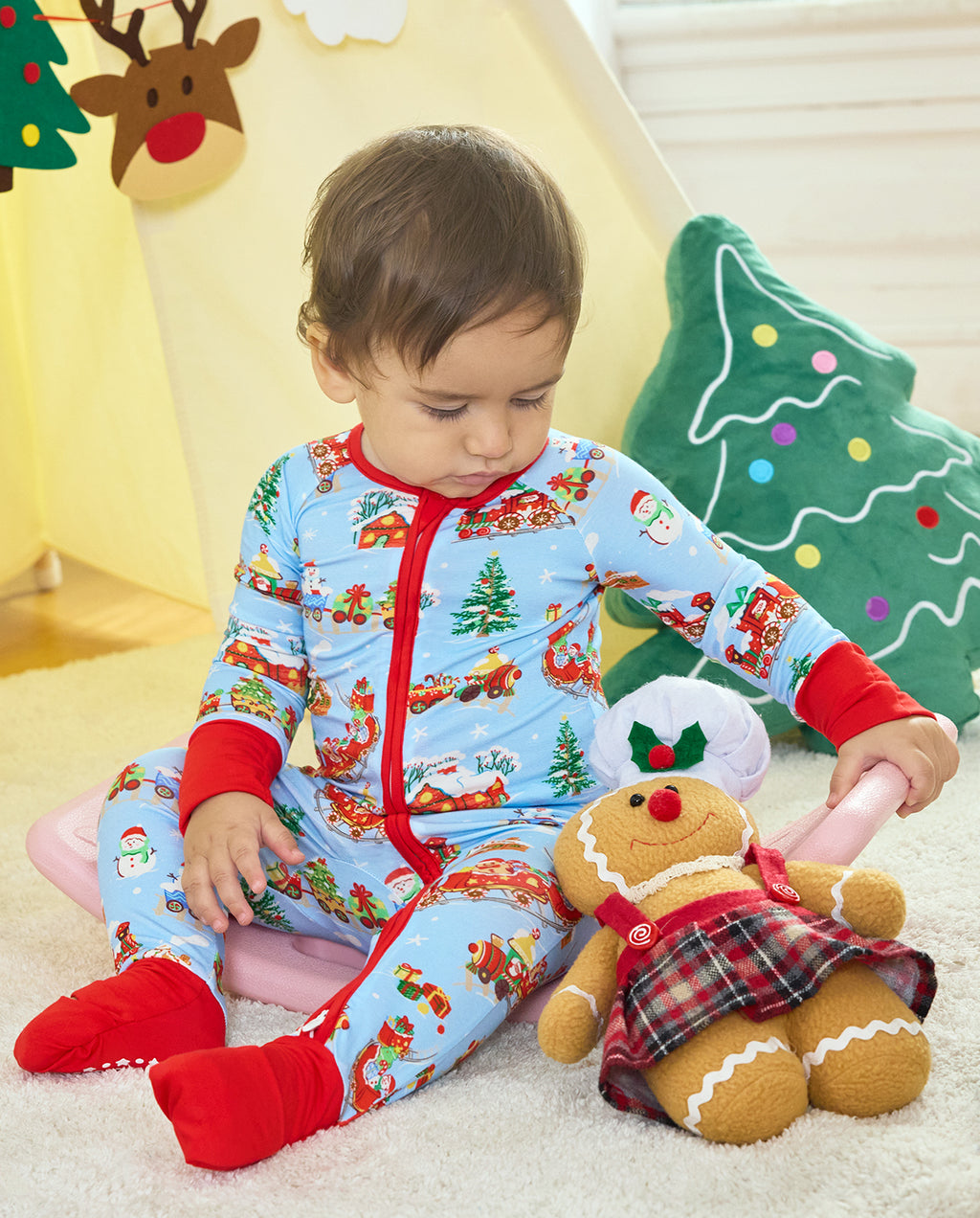 Child seated in the Christmas Trains Bamboo Zippy beside a gingerbread toy, with the red foot cuffs covering the feet.