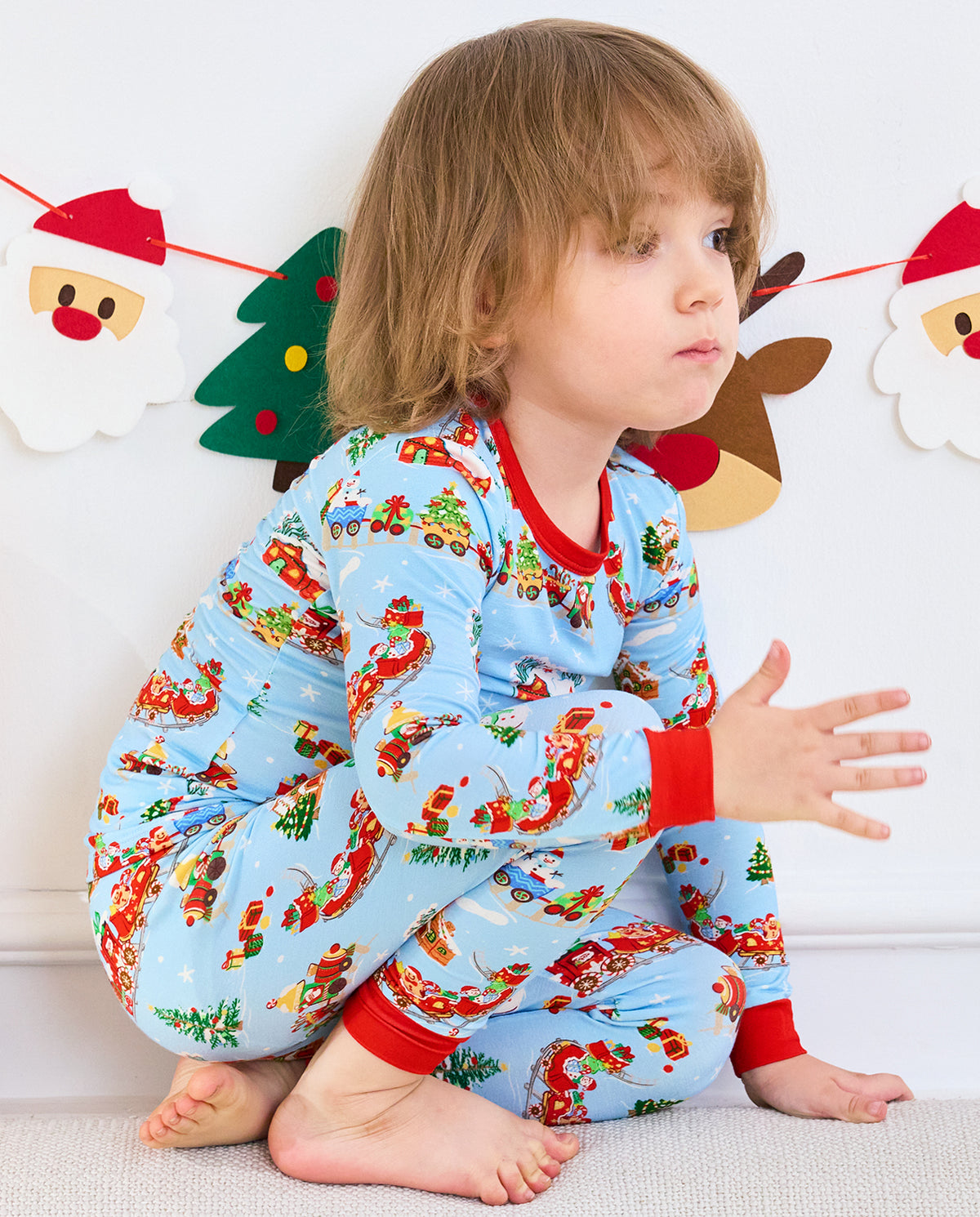 Child crouching on a seat in Christmas Trains pants with red ankle cuffs.