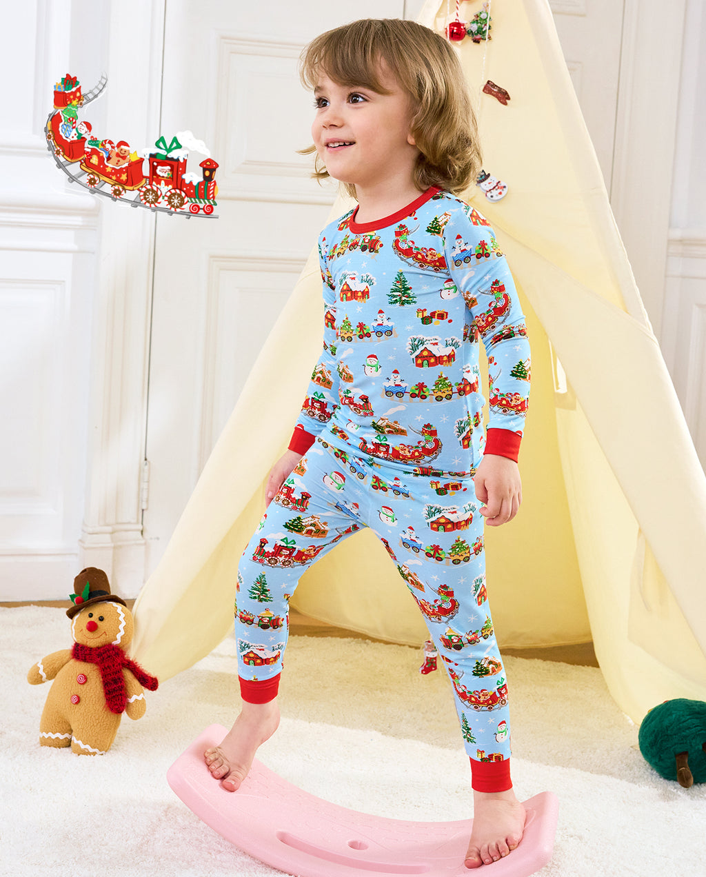 Child standing by a pink rocker in Christmas Trains pajamas, with a train illustration overlay.