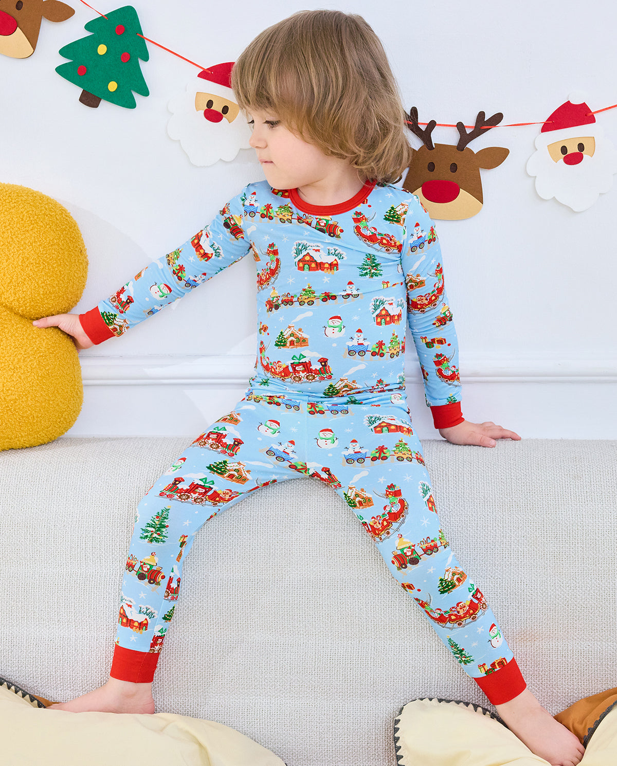 Child seated on a white sofa wearing the Christmas Trains pajama set.