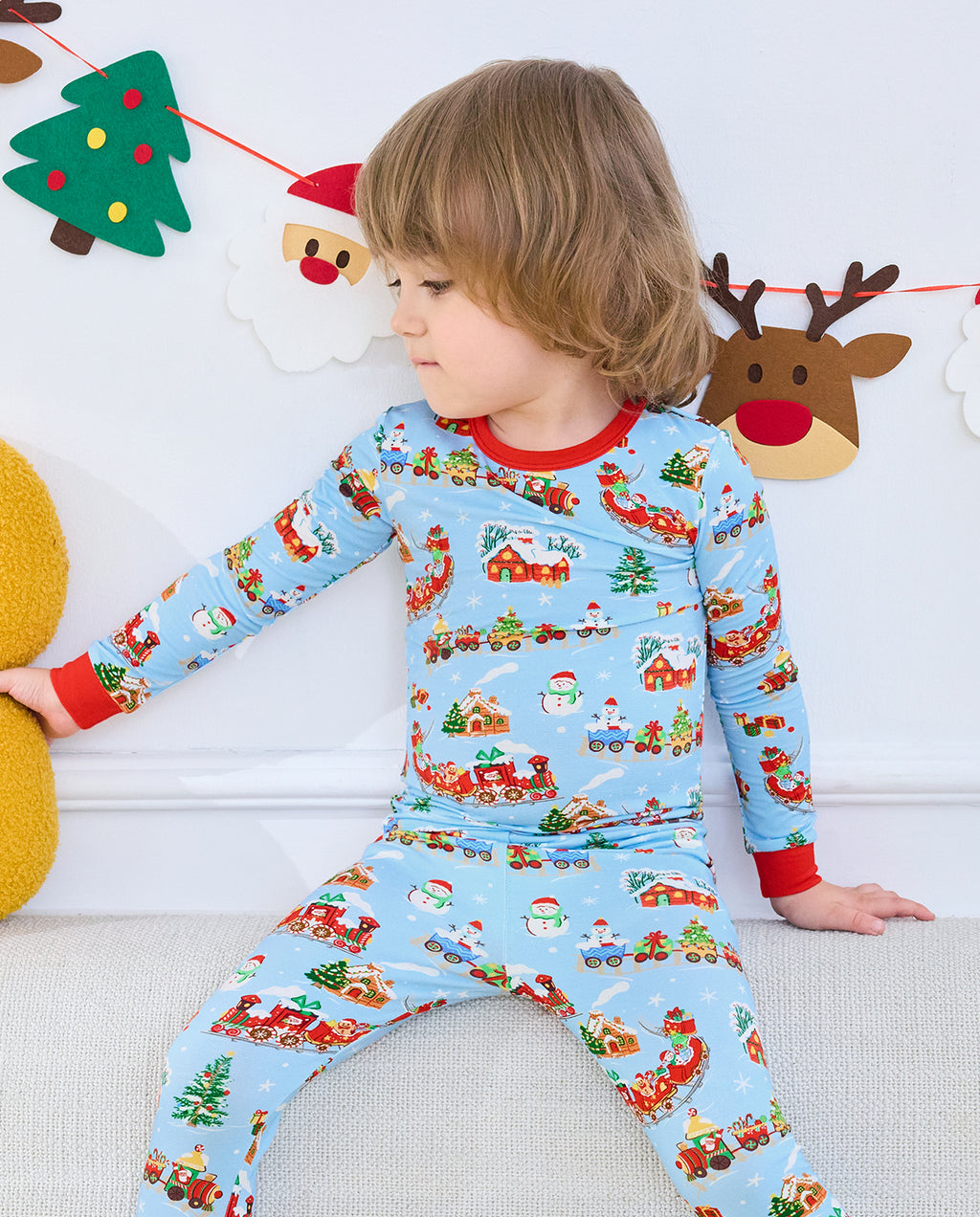 Side view of a seated child in Christmas Trains pajamas on a white sofa.