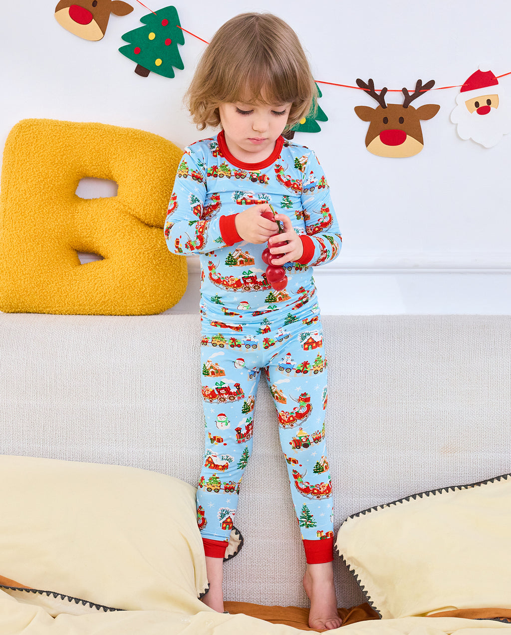 Child standing with a red toy in the Christmas Trains two-piece pajama set.