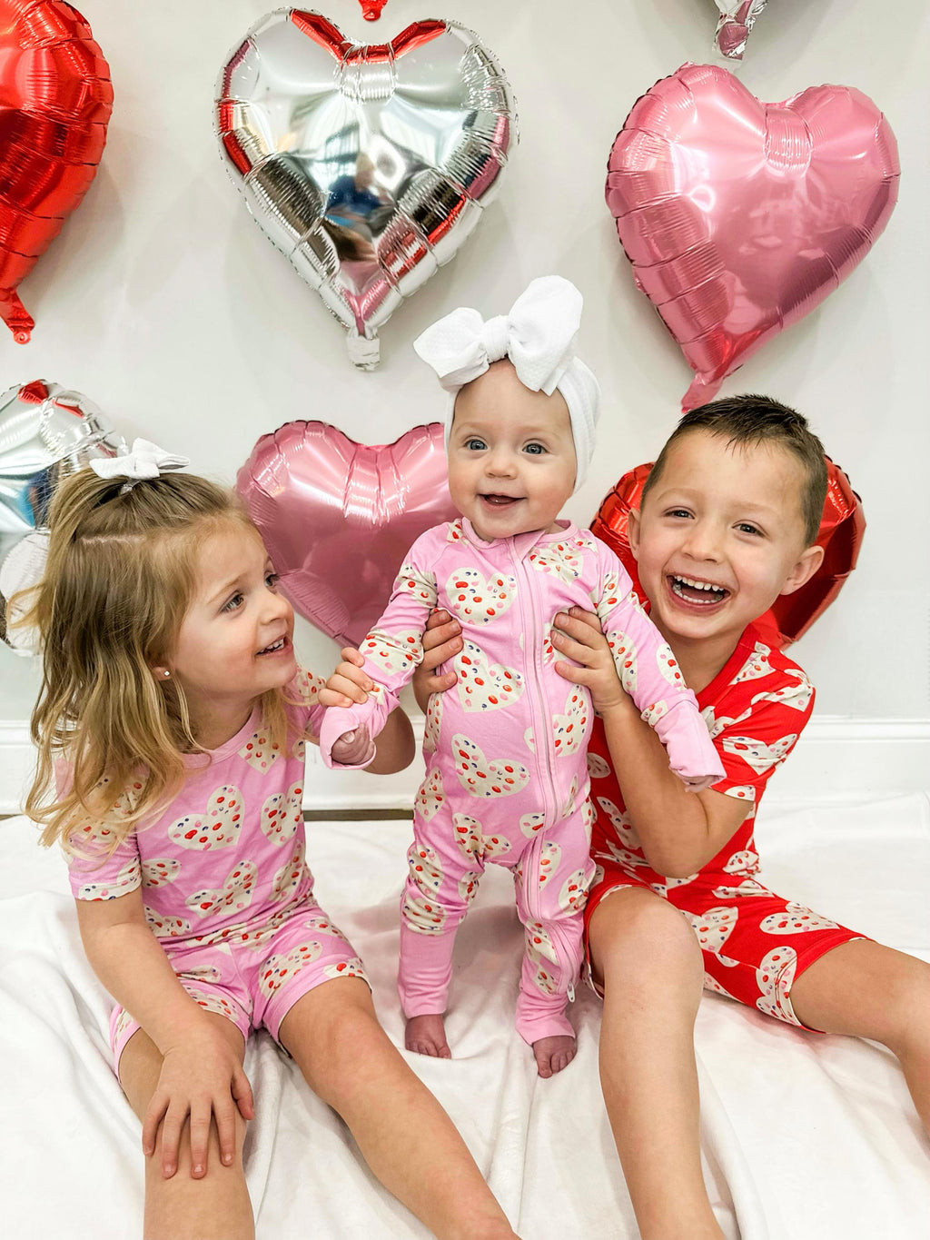 Three children wearing babee Reshinee Createe Cozee custom bamboo pajamas with pink and red heart prints