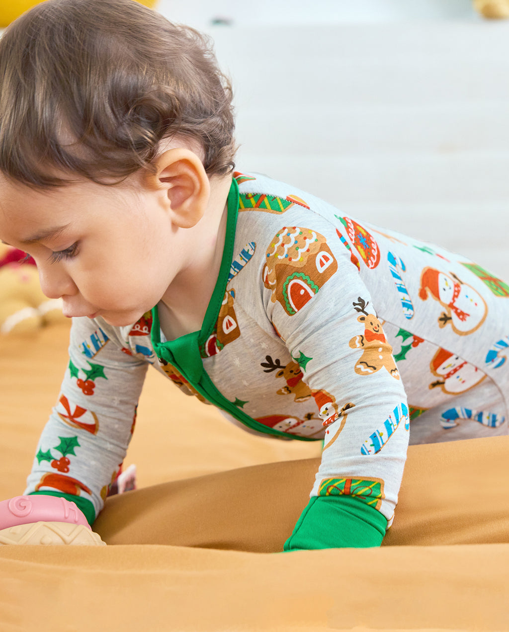 Close-up of a crawling baby in the Gingerbread Gala Bamboo Zippy, showing green sleeve cuffs and a gingerbread house print