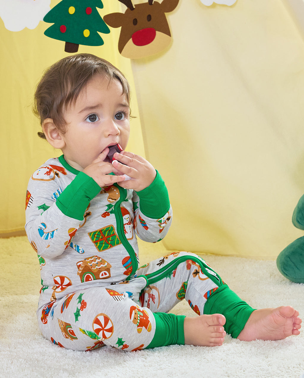 Baby sitting in the Gingerbread Gala Bamboo Zippy with green foot cuffs folded back and bare feet visible