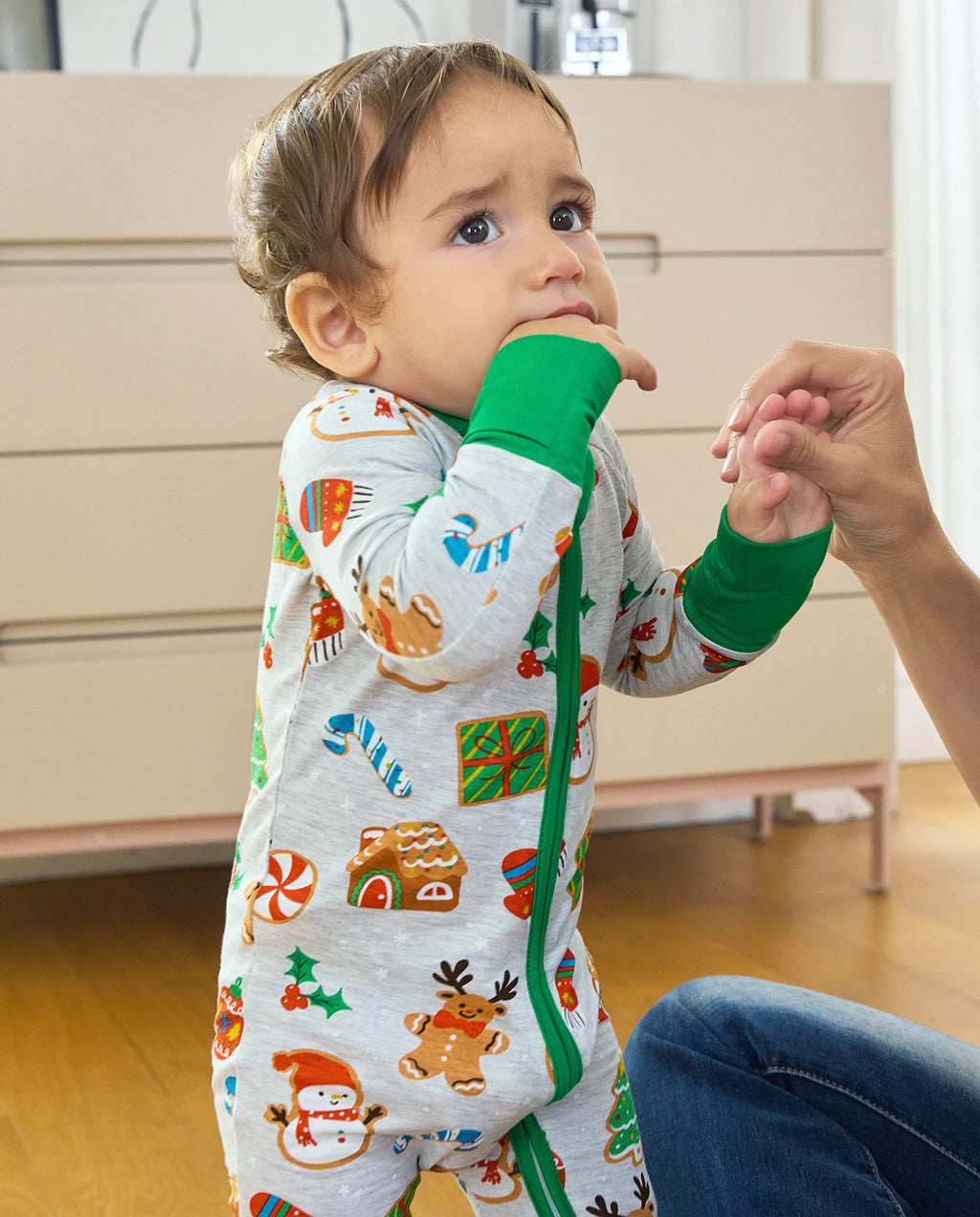 Baby holding an adult's hand in the Gingerbread Gala Bamboo Zippy, with green cuffs and a front zipper