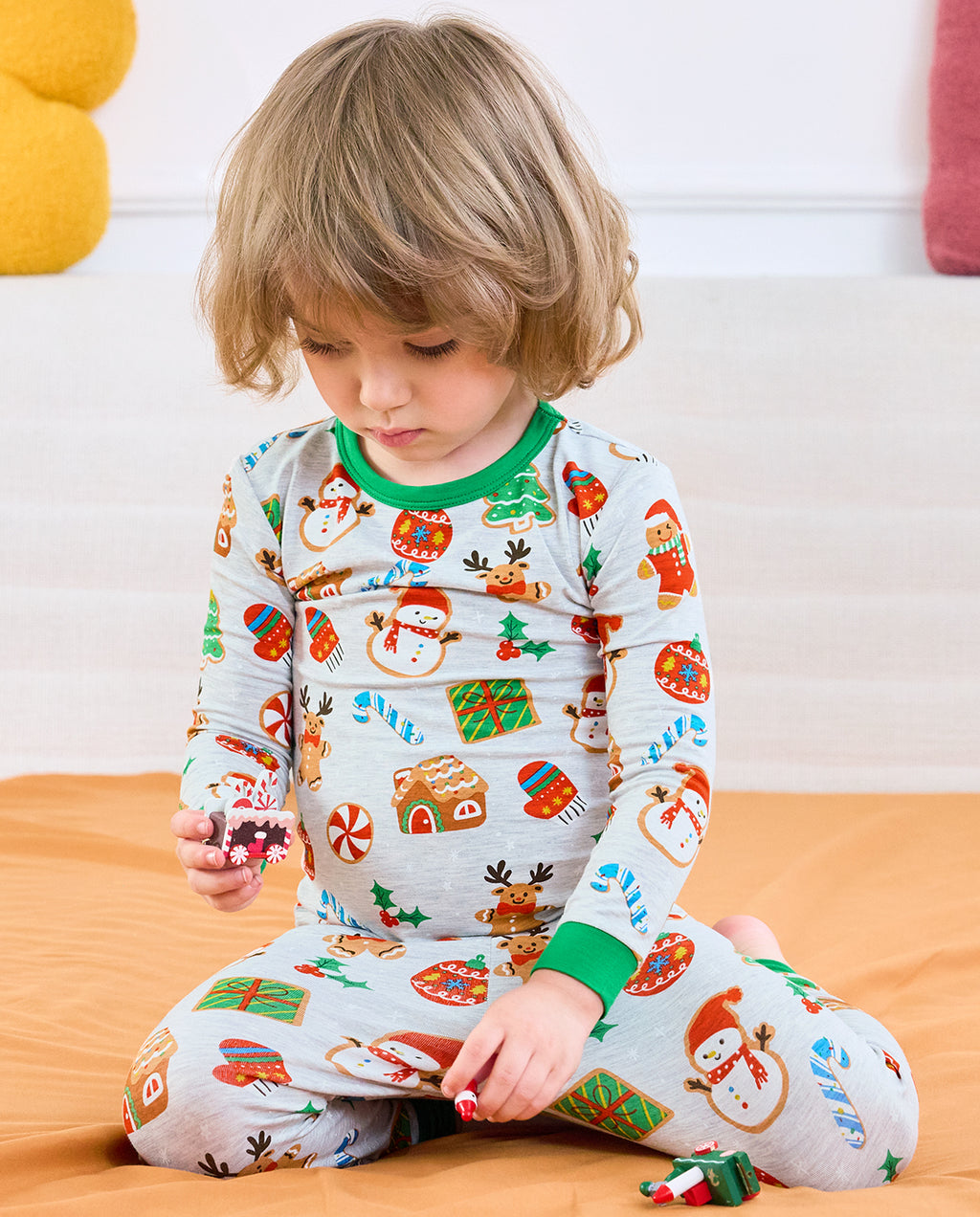 Child seated in Gingerbread Gala cookie-print pajamas with green neckline and cuffs