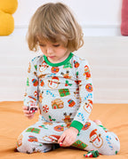 Child seated in Gingerbread Gala cookie-print pajamas with green neckline and cuffs