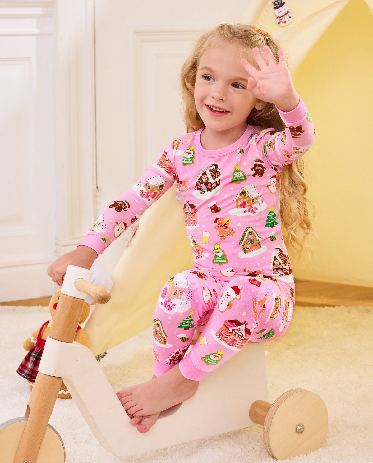 Child seated on a wooden tricycle in Gingerbread Lane pajamas.