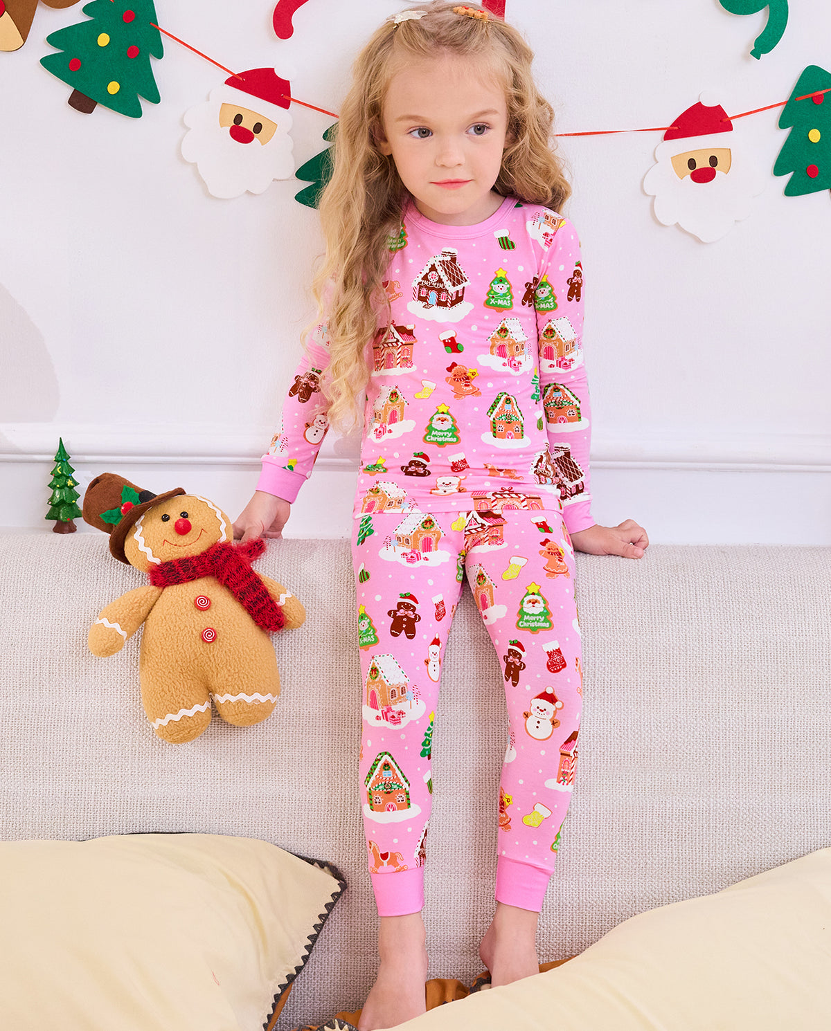 Child seated beside a gingerbread plush toy in Gingerbread Lane pajamas.