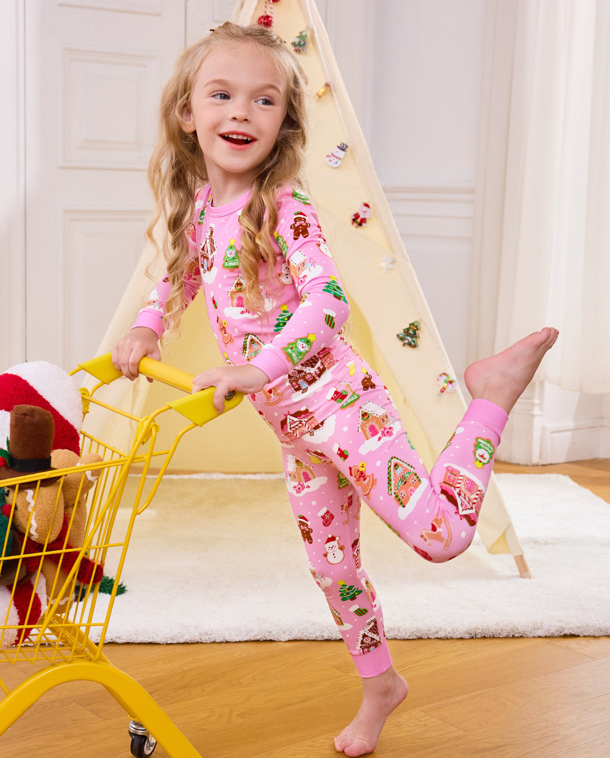 Child holding a yellow cart with one leg raised in Gingerbread Lane pajamas.