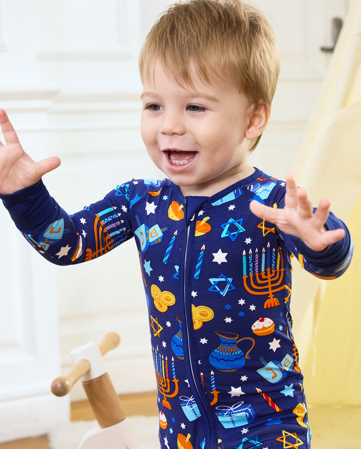 Close front view of a smiling child in the Hanukkah Magic zip-up romper.