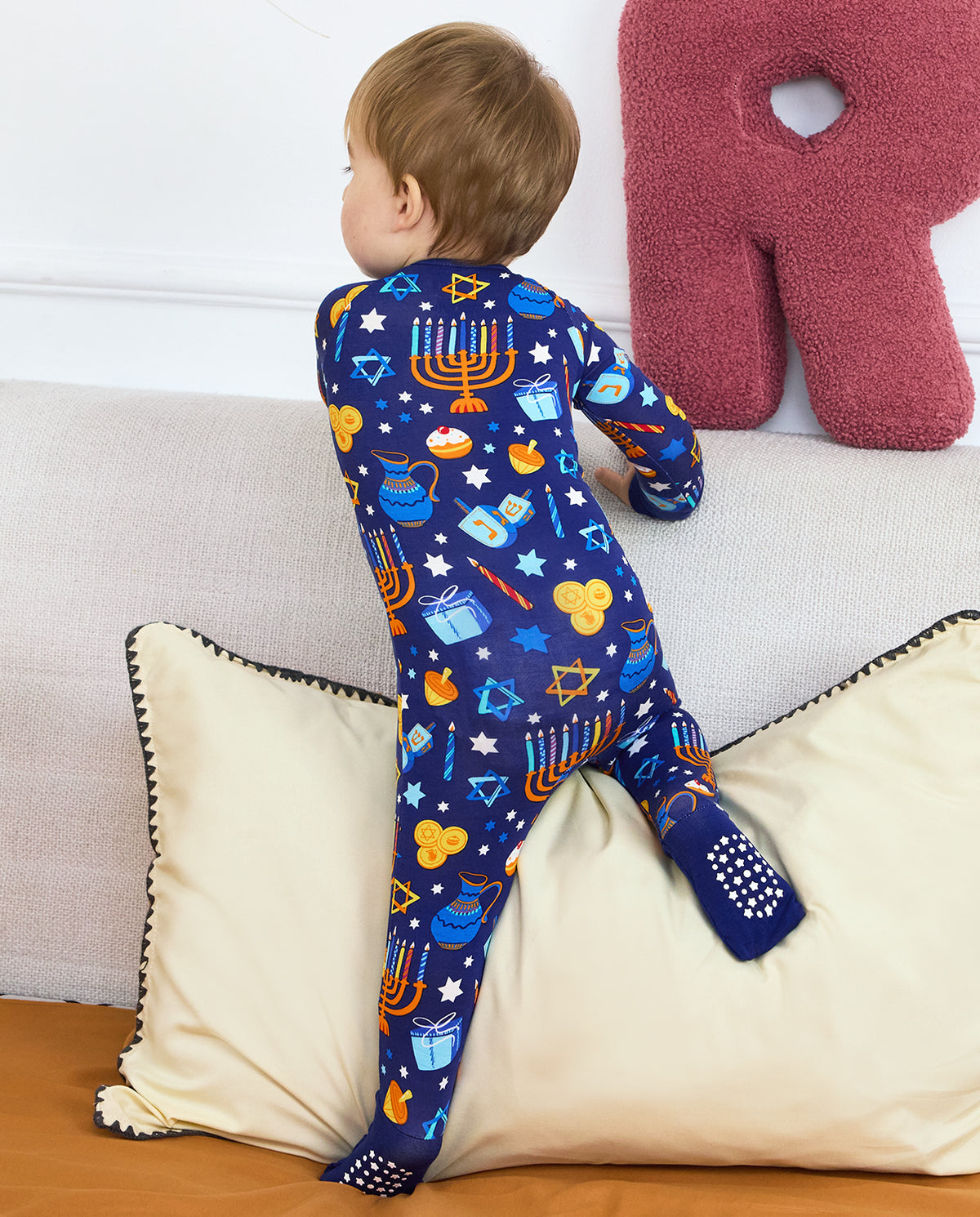 Rear view of a child standing on bedding in the navy Hanukkah Magic romper.