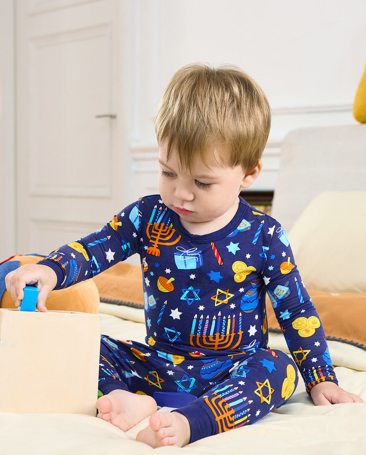 Child seated beside a wooden toy box in the Hanukkah Magic two-piece pajama set.