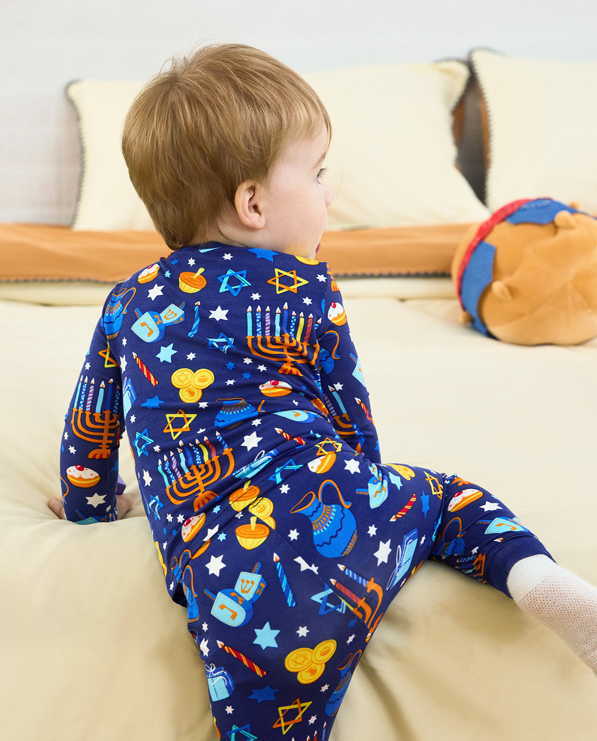 Rear view of a child seated on a sofa in the Hanukkah Magic pajama set.