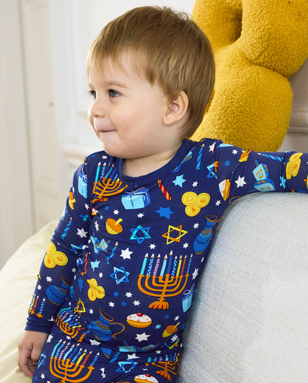 Side close view of a child leaning on a sofa in the Hanukkah Magic top.